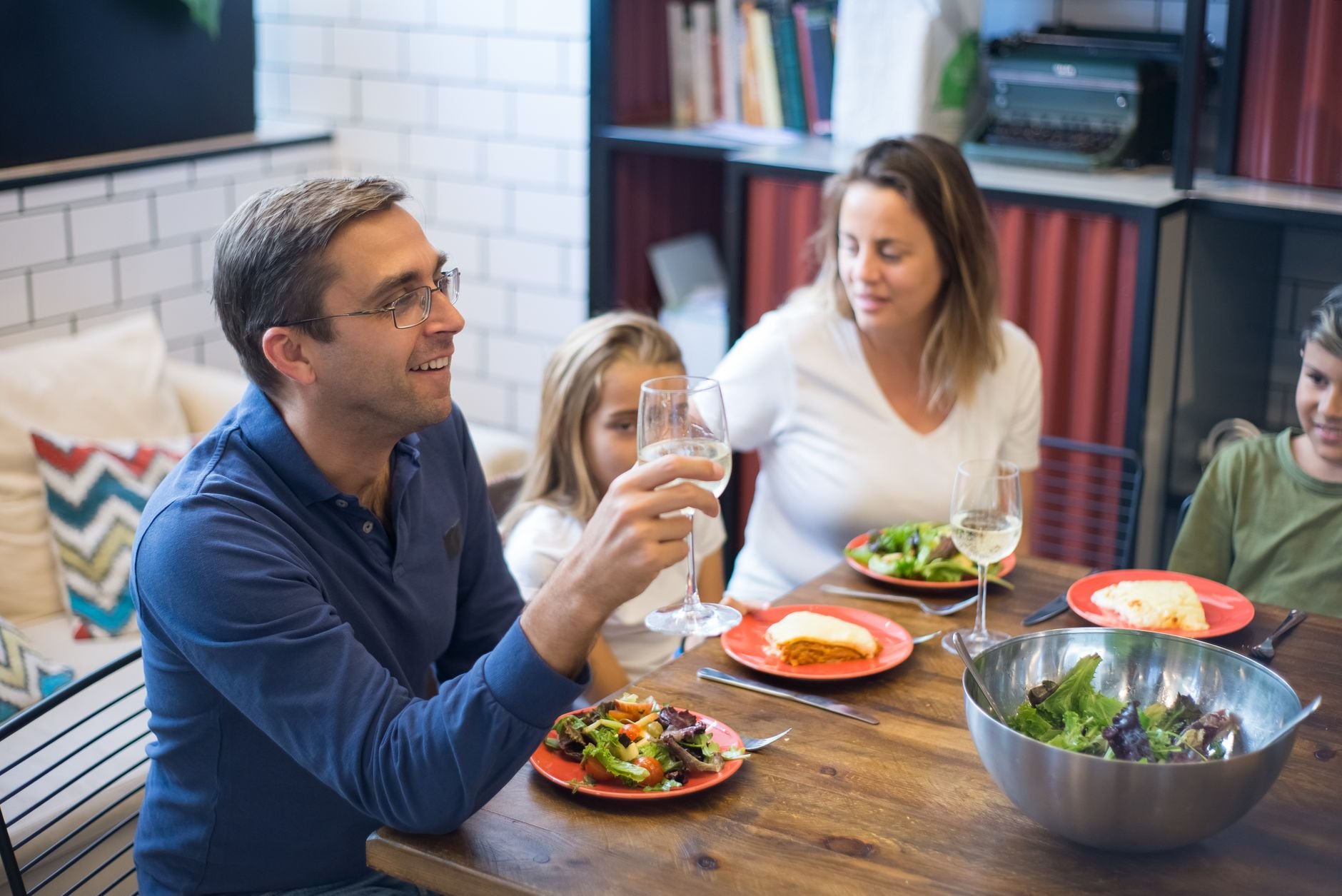A happy family of four enjoying a meal with salads and wine at home.